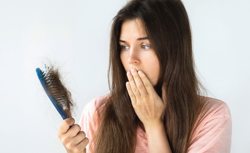 ragazza con in mano una spazzola piena di capelli caduti